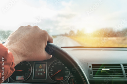 Driving car,road,hand of male driver on steering wheel,cloudy sunset sky, travel background.Close up,selective focus.Spring sunset landscape.