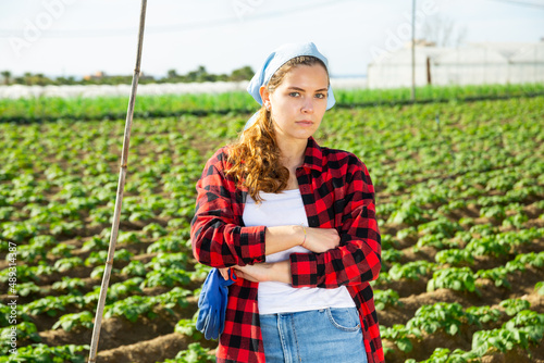 Portrait of confident skillful girl farmer posing on vegetable field of small farm during spring works..