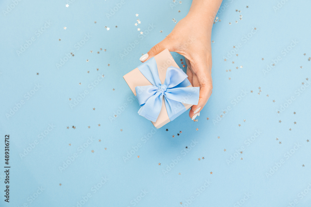 A hand holds a blue gift box on a blue background with glitter stars. top view, copy space A hand holds a blue gift box on a blue background with glitter stars. top view, copy space