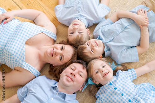 Portrait happy caucasian family posing on floor house  lying on carpet and approaching  smiling cheerfully  top view. Positive european father  mother and daughter and two brothers hugging