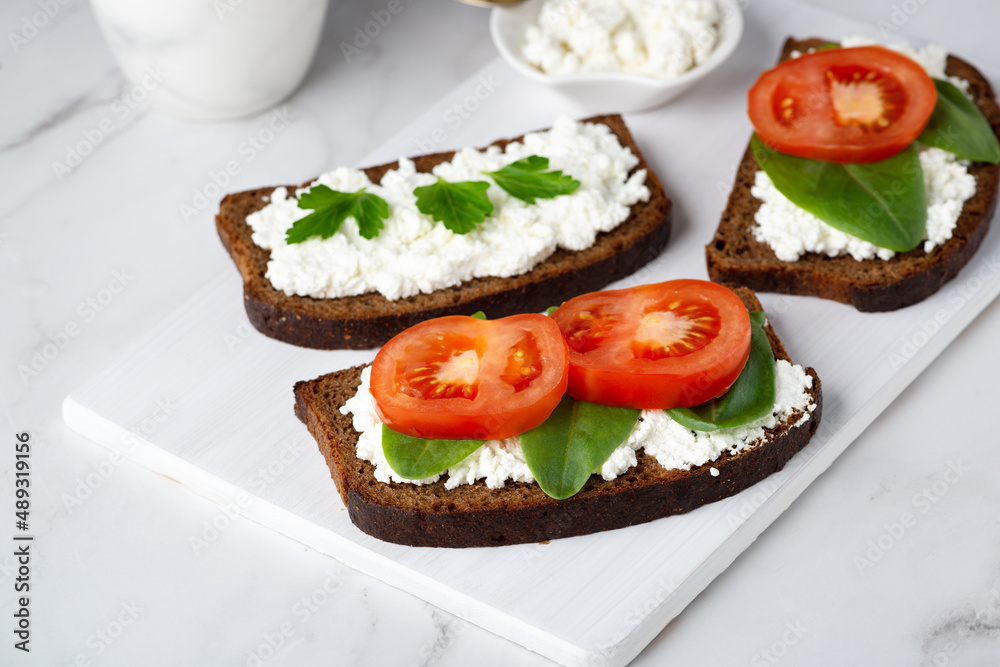Slice of rye bread with cottage cheese and tomatoes on a wooden cutting board