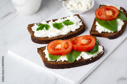 Slice of rye bread with cottage cheese and tomatoes on a wooden cutting board