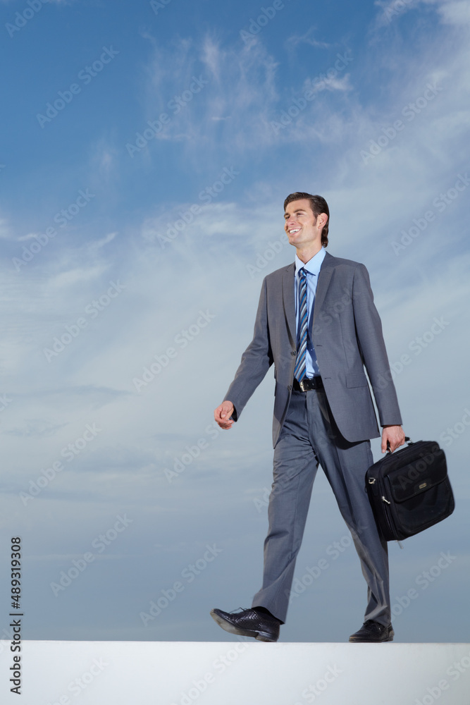 Strolling towards success. A young businessman carrying his briefcase against a blue sky. Strolling towards success. A young businessman carrying his briefcase against a blue sky.