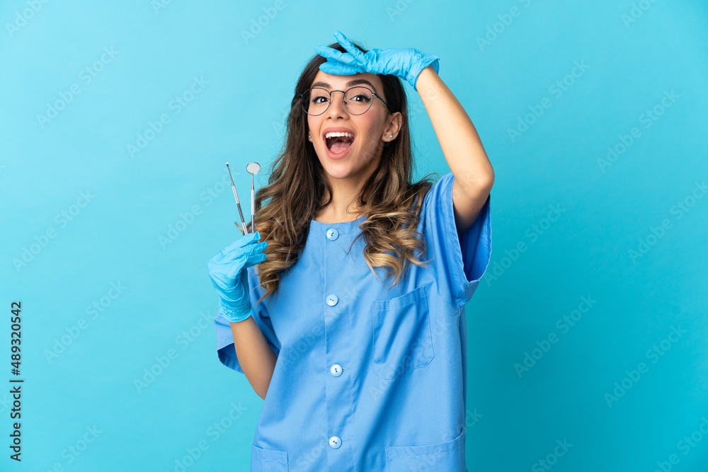 Woman dentist holding tools over isolated on blue background doing surprise gesture while looking to the side Woman dentist holding tools over isolated on blue background doing surprise gesture while looking to the side