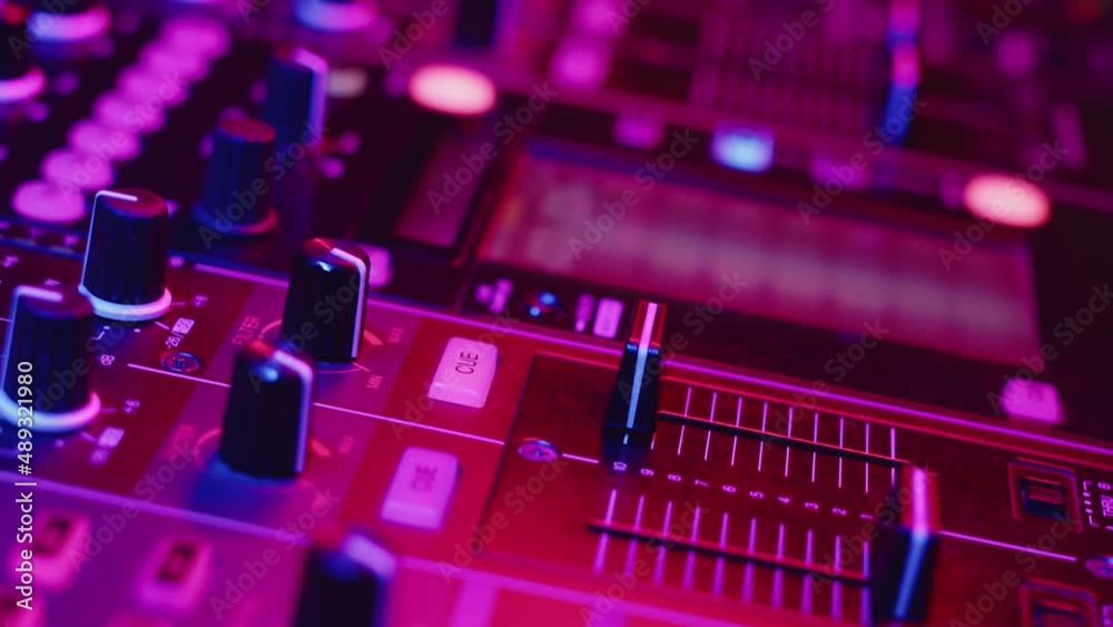 Hand of professional DJ adjusts cue slider on fader in digital music console in neon light nightclub, closeup. Concept professional musical accompaniment of party Hand of professional DJ adjusts cue slider on fader in digital music console in neon light nightclub, closeup. Concept professional musical accompaniment of party