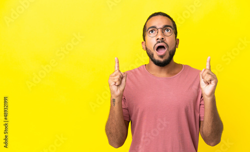Young latin man isolated on yellow background surprised and pointing up