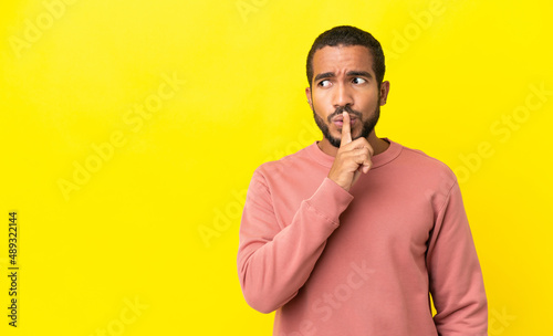 Young latin man isolated on yellow background showing a sign of silence gesture putting finger in mouth