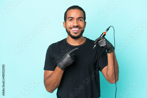 Tattoo artist Ecuadorian man isolated on blue background pointing to the side to present a product