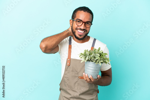 Gardener latin man holding a plant isolated on blue background laughing