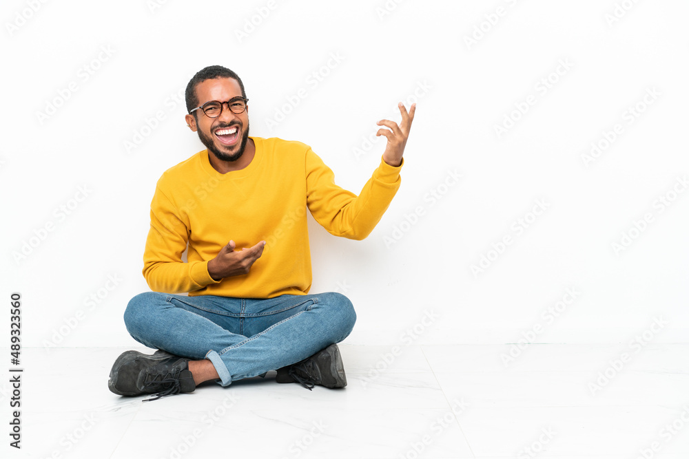 Young Ecuadorian man sitting on the floor isolated on white wall making guitar gesture Young Ecuadorian man sitting on the floor isolated on white wall making guitar gesture