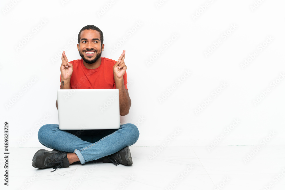 Young Ecuadorian man with a laptop sitting on the floor isolated on white background with fingers crossing Young Ecuadorian man with a laptop sitting on the floor isolated on white background with fingers crossing