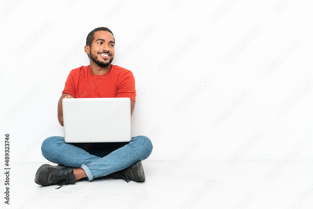 Young Ecuadorian man with a laptop sitting on the floor isolated on white background with arms crossed and happy Young Ecuadorian man with a laptop sitting on the floor isolated on white background with arms crossed and happy