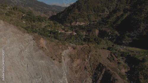 Village on the edge of a cliff in a mountainous region valley surrounded by trees aerial reversing revealing huge rock wall Kabayan Benguet Philippines photo