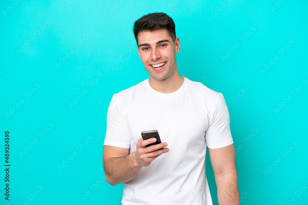 Young caucasian man isolated on blue background using mobile phone Young caucasian man isolated on blue background using mobile phone