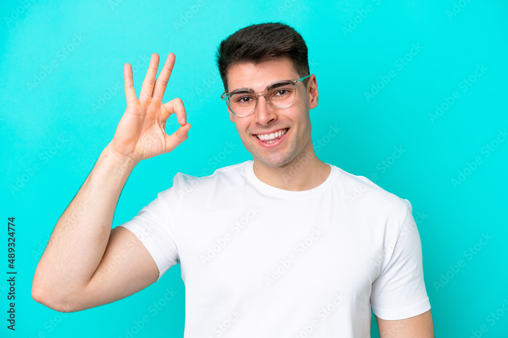 Young caucasian man isolated on blue background With glasses and doing OK sign Young caucasian man isolated on blue background With glasses and doing OK sign