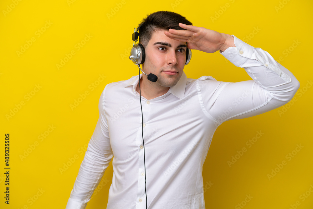 Telemarketer caucasian man working with a headset isolated on yellow background looking far away with hand to look something Telemarketer caucasian man working with a headset isolated on yellow background looking far away with hand to look something