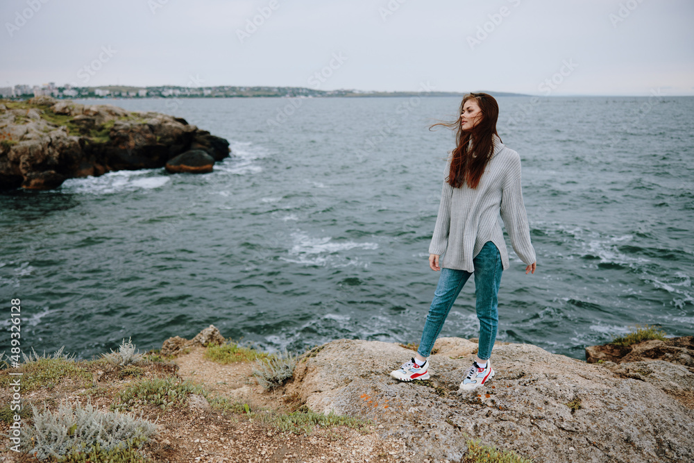 woman in a gray sweater stands on a rocky shore nature Relaxation concept