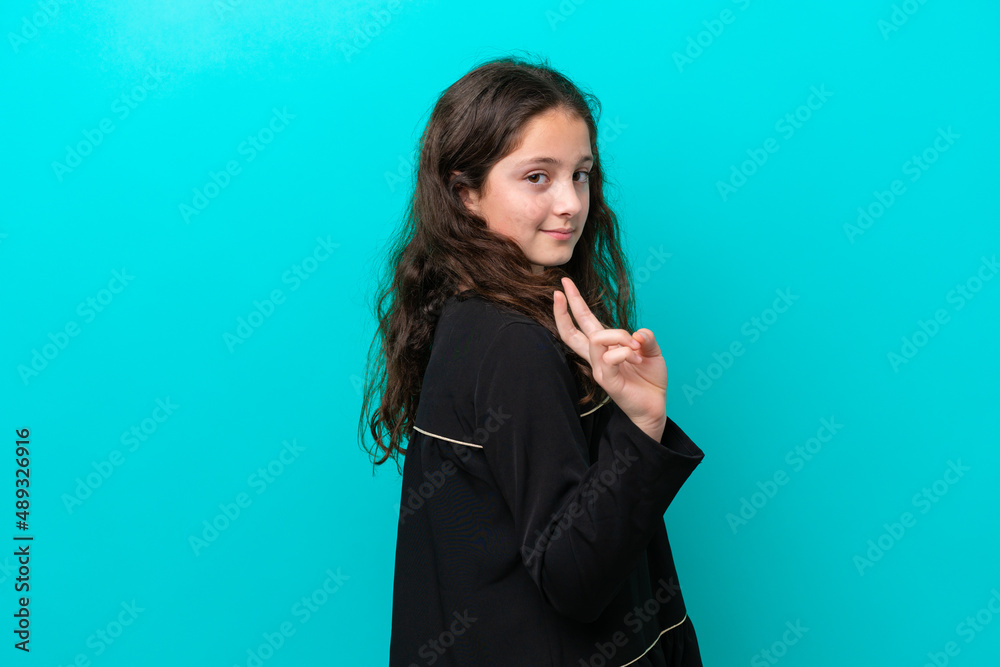 Little girl isolated on blue background smiling and showing victory sign