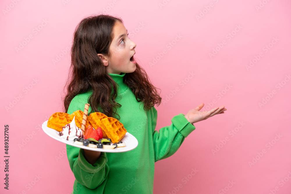 Little caucasian girl holding waffles isolated on pink background with surprise facial expression Little caucasian girl holding waffles isolated on pink background with surprise facial expression