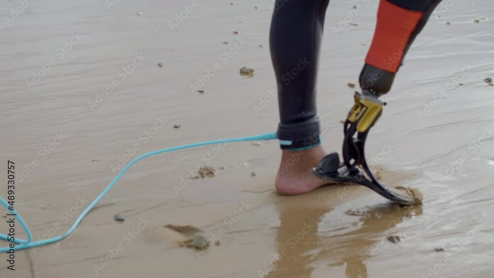 Fit surfer with bionic leg walking along seashore. Tracking shot of man