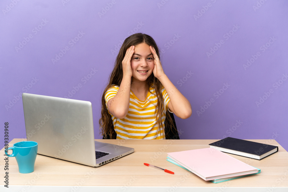 Little student girl in a workplace with a laptop isolated on purple background laughing Little student girl in a workplace with a laptop isolated on purple background laughing