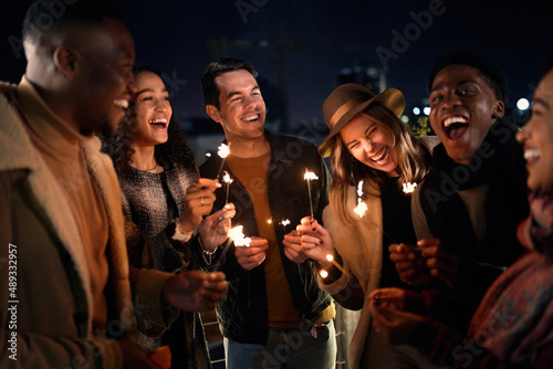 Diverse group of friends laughing at a party on a rooftop terrace. Nightlife in the city, Lighting Sparklers
