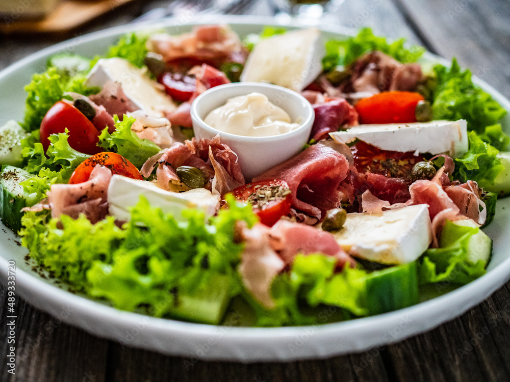 Tasty salad - prosciutto di Parma, camembert and fresh, green vegetables on wooden table
