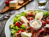 Tasty salad - prosciutto di Parma, camembert and fresh, green vegetables on wooden table

