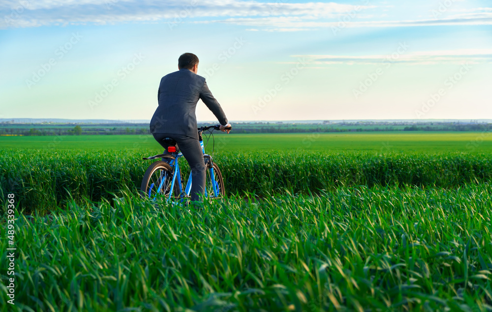 one businessman with red folder for reports or documents rides a bicycle through a green grass field, dressed in a business suit, beautiful nature in summer, business concept one businessman with red folder for reports or documents rides a bicycle through a green grass field, dressed in a business suit, beautiful nature in summer, business concept