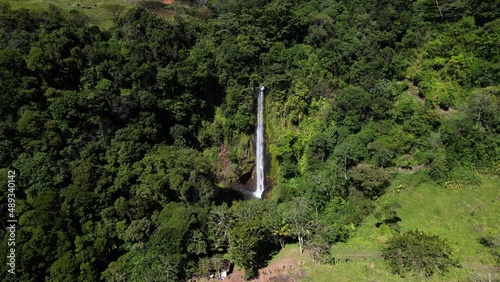 Panning wide drone perspective of tall waterfall surrounded by rainforest green vegetation, Monte verde photo