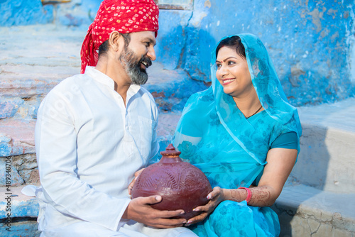 Happy traditional Indian couple holding clay money box or gullak in hand. Smiling woman wearing sari and man wear red turban with traditional piggy bank, investment and banking concept. photo