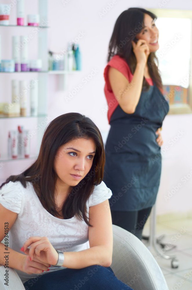 Time for a new hairdresser. A young woman looking annoyed as she waits for her stylist to finish a personal call. Time for a new hairdresser. A young woman looking annoyed as she waits for her stylist to finish a personal call.