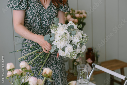 Florist makes a bouquet for the holiday in the workshop in a green dress. White carnation flowers