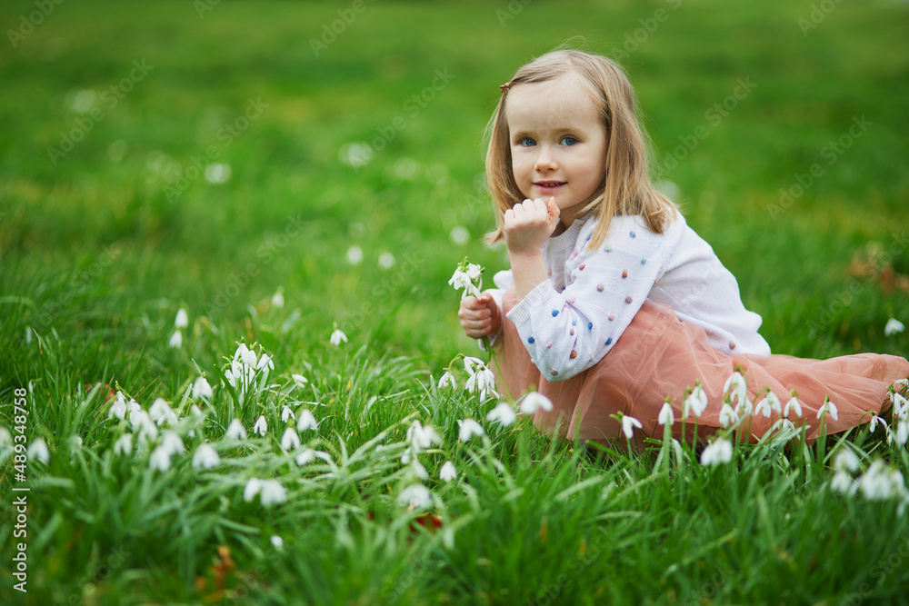 Cute preschooler girl in pink tutu skirt sitting in the grass with many snowdrop flowers in park or forest on a spring day Cute preschooler girl in pink tutu skirt sitting in the grass with many snowdrop flowers in park or forest on a spring day