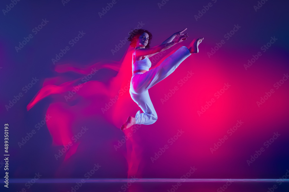 Young sportive beautiful girl, hip-hop dancer dancing hip hop isolated on purple background in pink neon light. Youth culture, style and fashion, action.