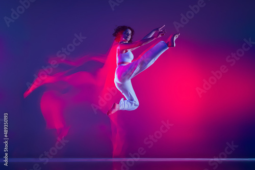 Fototapeta Naklejka Na Ścianę i Meble -  Young sportive beautiful girl, hip-hop dancer dancing hip hop isolated on purple background in pink neon light. Youth culture, style and fashion, action.
