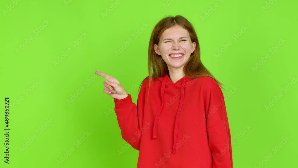 Young woman pointing finger to the side and presenting a product over isolated background. Green screen chroma key Young woman pointing finger to the side and presenting a product over isolated background. Green screen chroma key