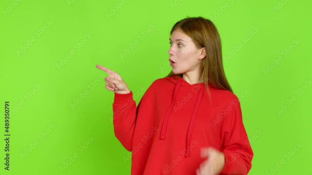 Young woman pointing to the side and presenting a product while smiling over isolated background. Green screen chroma key Young woman pointing to the side and presenting a product while smiling over isolated background. Green screen chroma key