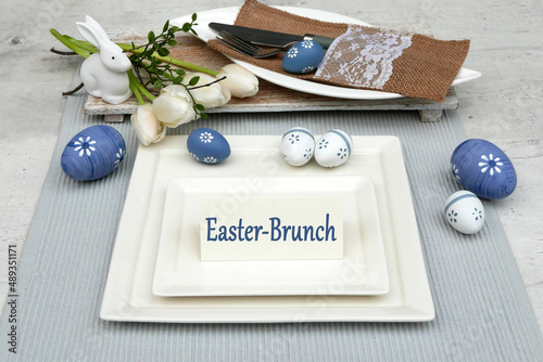 Covered Easter table with plates, cutlery, flowers and the text Easter Brunch on a card.
