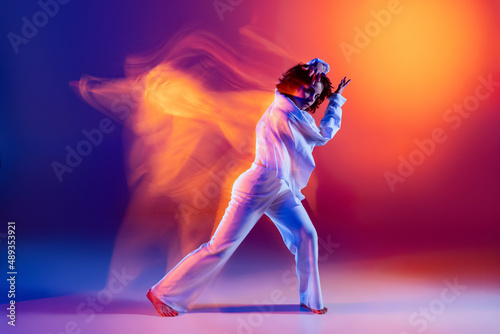 Street dancing. Image of flexible young girl, hip-hop dancer in white outfit dancing hip hop isolated on blue background in yellow neon light. Youth culture, style and fashion, action. © master1305