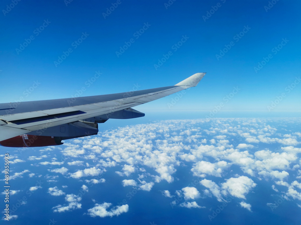 View from the porthole on the wing of an airplane with a red aircraft engine flying over beautiful white clouds and the sea. View from the porthole on the wing of an airplane with a red aircraft engine flying over beautiful white clouds and the sea.