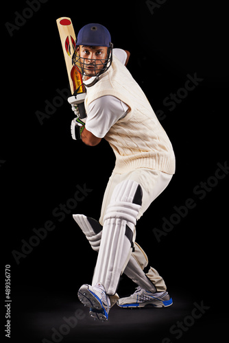 Hes got some talent with the bat. A cropped shot of an ethnic young man in cricket attire isolated on black. photo