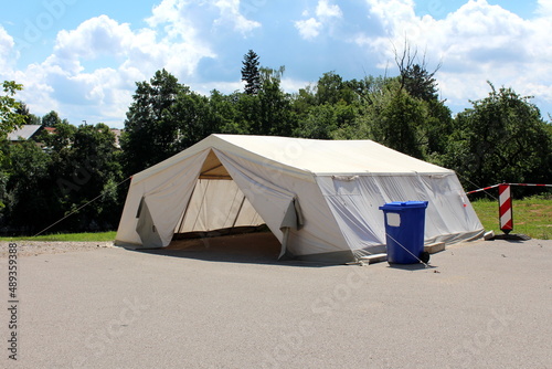 White field hospital tent built by military on paved parking lot and used for COVID-19 coronavirus outdoor testing next to plastic blue garbage container used for medical waste