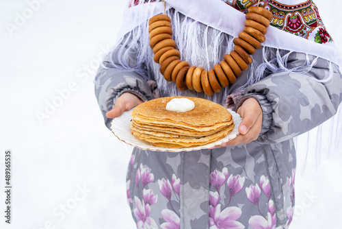 Traditional russian bagels for tea on a rope and pancakes on a plate in hand, Russian treat, Maslenitsa (Shirokaya Shrovetide) in Russia. photo