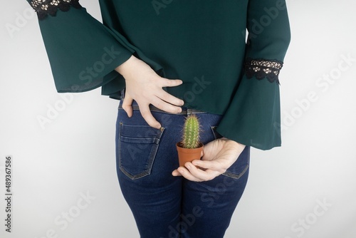 Concept. A woman holds a cactus as a symbol of rectal pain. Varicose veins of the lower intestine. Pain in the rectum, hemorrhoids and pain in the excretory system of the body. Proctology
