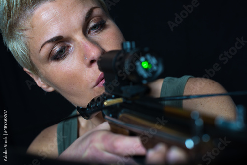 Leinwand Poster Young woman shooting with crossbow isolated on black background.