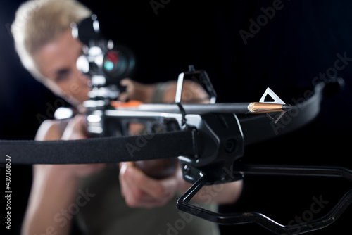 Young woman shooting with crossbow isolated on black background.