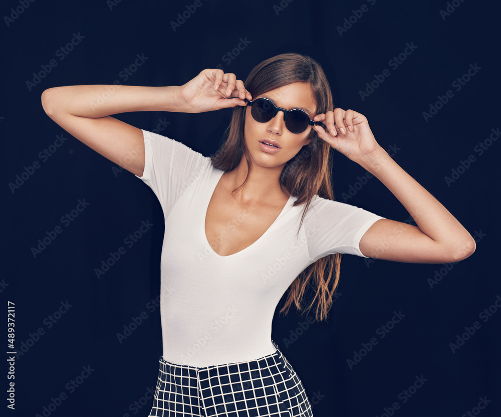 Keeping it cool. Studio shot of an attractive young woman holding her sunglasses.