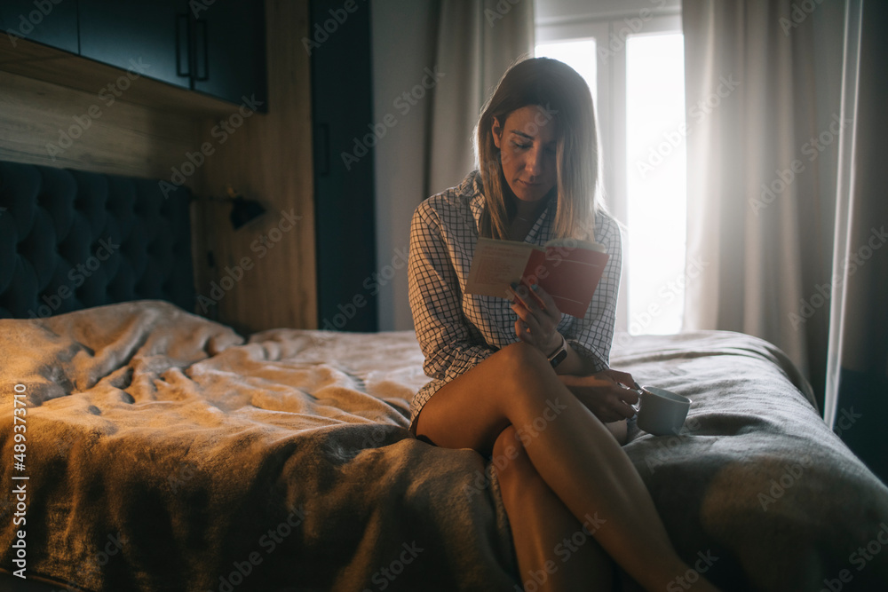 Woman sitting on bed and reading the book and enjoy coffee Woman sitting on bed and reading the book and enjoy coffee