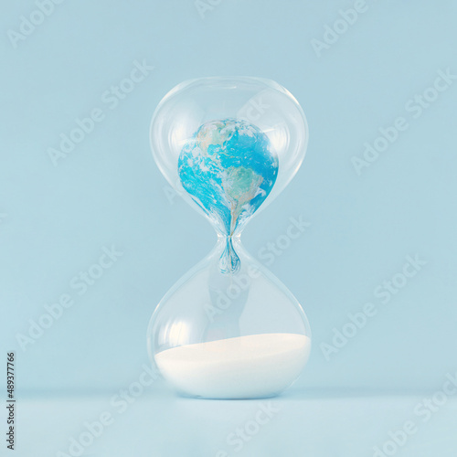 Close-up of planet Earth melting in hourglass on pastel blue background. Minimal creative concept of dystopian future. Anti-war idea, climate change or global pollution. The world provided by NASA.